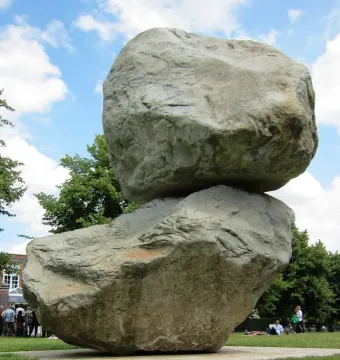 Rock on Top of Another Rock stacked on a grassy lawn with trees and people in the background