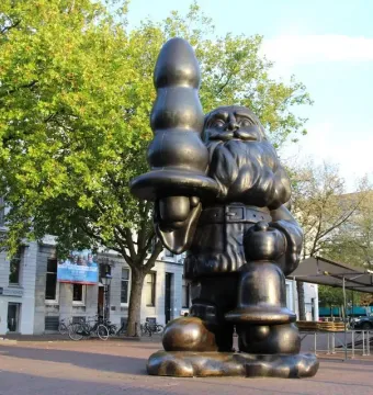 Dark metallic Santa Claus sculpture holding an abstract elongated object in one hand and a smaller object in the other.