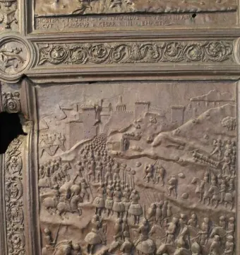 Close-up of the Bronze Gate showing a bas-relief battle scene with soldiers, horses, and a fortified city.