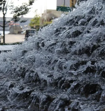 Cascading water over dark tiers with a street and parked cars blurred in the background near the National Katyń Memorial.