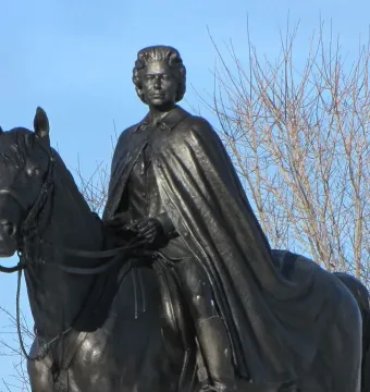 Elizabeth II equestrian statue showing a dark bronze monarch on horseback against a pale blue sky.