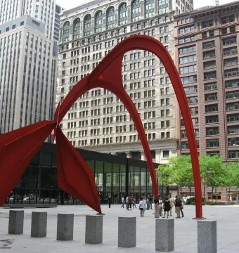 Flamingo, a large bright red abstract sculpture in a city plaza with tall buildings behind it.