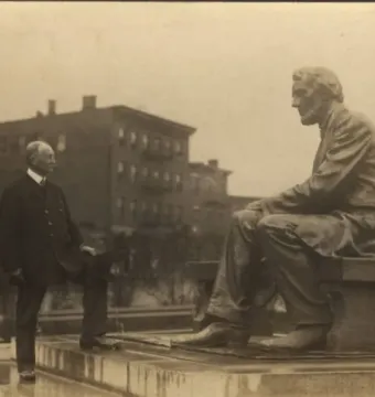A man in a suit stands beside the Seated Lincoln statue with one foot on a low platform, looking toward the sculpture.