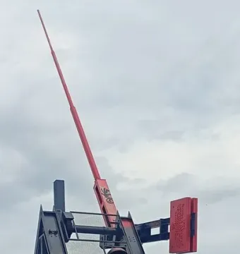 Prague Metronome mechanism with a red arm and counterweight against a cloudy sky.