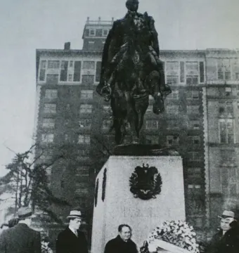 Simón Bolívar equestrian statue on a stone pedestal with men gathered below and a floral wreath at its base.