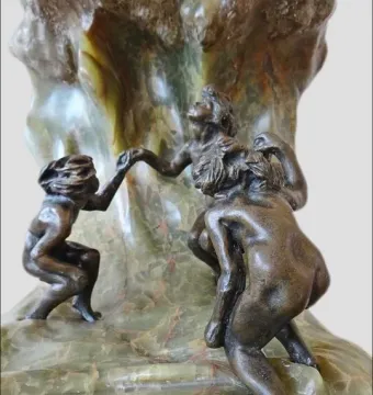 The Wave sculpture with three dark bronze nude figures holding hands on a veined stone base.