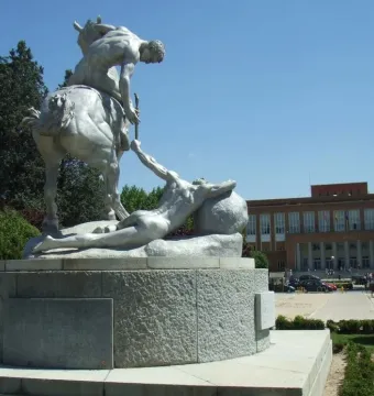 The Torch Bearers monument shows a nude rider on horseback passing a torch to a prone figure on a circular pedestal.