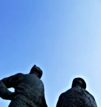 Two Working Men sculpture silhouetted against a clear blue sky, with one figure wearing a cap.