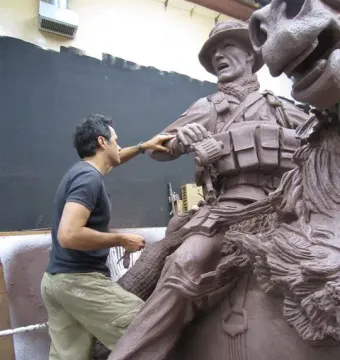 A man stands beside a reddish-brown clay model of America\'s Response Monument, touching the soldier on horseback sculpture.