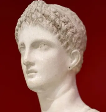 Marble bust of Artemis Diadoumena in profile against a red background, with short textured hair and draped shoulders.