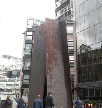 The Fulcrum sculpture stands in an urban plaza beside pedestrians and modern office buildings.