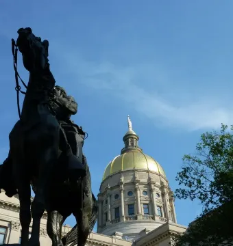John Brown Gordon statue silhouetted against the Georgia State Capitol dome and blue sky.