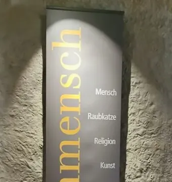 Banner for the Löwenmensch exhibit with golden vertical lettering and a list of related terms on a wall.
