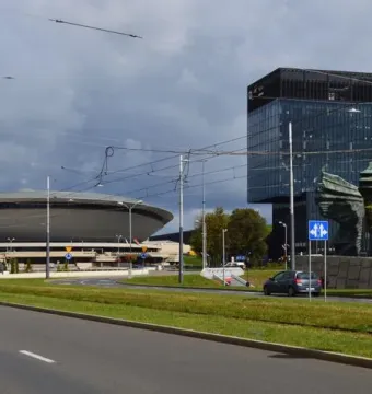 Silesian Insurgents\' Monument seen behind trees and road signs, with a glass skyscraper in the background.