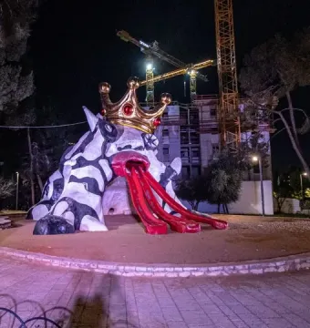 The Golem sculpture with a crown at night, showing a black-and-white patterned figure and three red ramps extending from its mouth.
