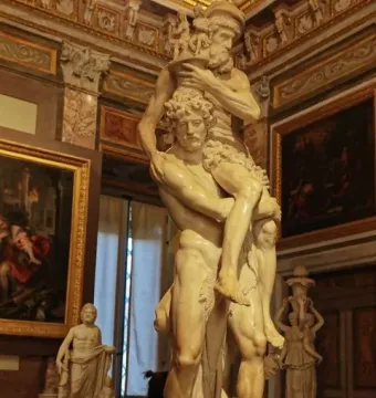 Marble sculpture of Aeneas carrying Anchises on his shoulders with Ascanius beside him in a museum room.