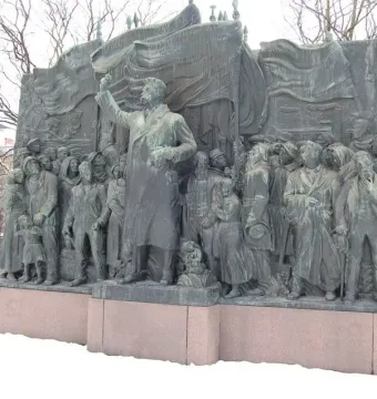 The Branting Monument in a snowy square, showing a bronze figure addressing a crowd with raised arm and draped flag-like forms behind.