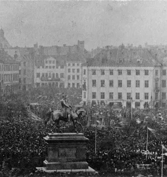 Frederick VII’s equestrian statue stands on a tall pedestal in a crowded city square surrounded by European-style buildings.
