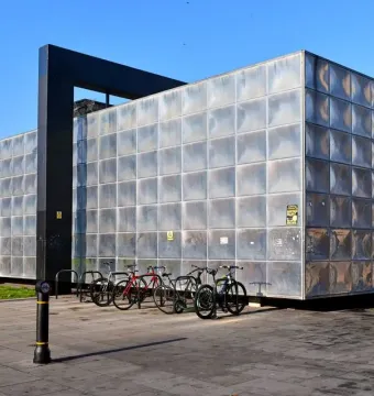 Michael Faraday Memorial with reflective metal panels and a dark rectangular archway, with bicycles parked in front.