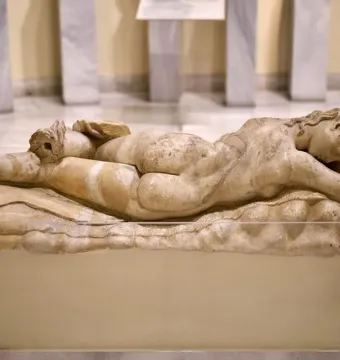 Ancient marble Sleeping Maenad reclining on a pedestal in a museum display.
