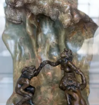 The Wave sculpture with three intertwined bronze figures beside a tall marbled stone form.