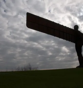 The Angel of the North sculpture standing on a grassy hill against a cloudy sky.