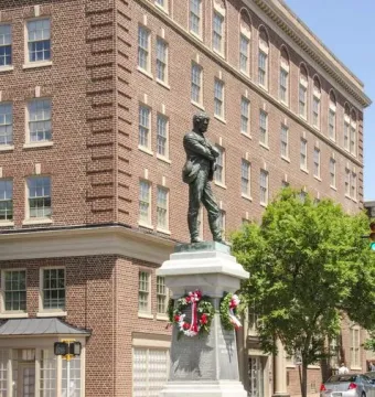 Appomattox bronze statue of a man with crossed arms on a tall stone pedestal at a street intersection.