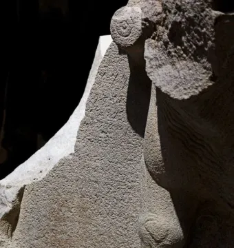 Close-up of the Çineköy inscription carved into light-colored stone, with incised symbols and a sculpted form in strong shadow.