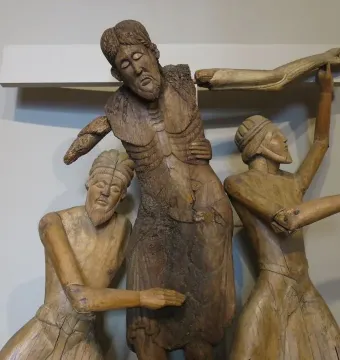 Central figures from the Descent from the Cross sculpture, with a bearded man supported by two robed figures beside a white cross.