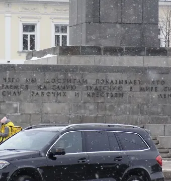 Lower part of the Lenin Monument with Russian text carved into the stone base, with snow falling nearby.