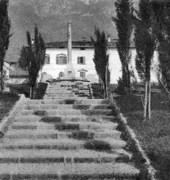 A long stone staircase leads up to the Lighthouse of Lierna, framed by slender trees with mountains in the background.