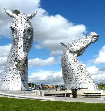 The Kelpies horse head sculptures beside water under a blue sky with clouds.