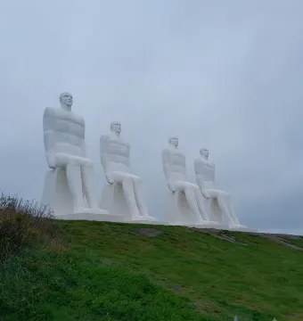 The Man by the Sea sculpture with four white seated figures on a grassy slope under a grey sky.