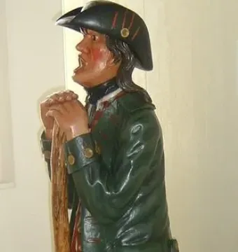 Aschaffenburger Maulaff sculpture of a painted man in a dark green coat and black hat, holding a walking stick.