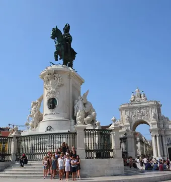 The Equestrian Statue of Joseph I on a white stone pedestal in a public square, with a grand archway and yellow buildings behind it.
