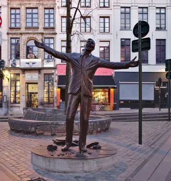 Jacques Brel memorial bronze statue by Tom Frantzen, shown with arms outstretched on a cobblestone square in Brussels.
