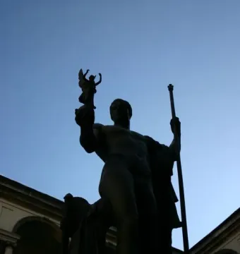 Napoleon as Mars the Peacemaker statue silhouetted against a blue sky, with arches and columns behind it.