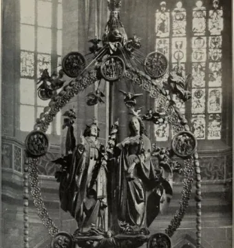 Angelic Salutation, an ornate sculptural ensemble with an angel and woman standing inside a circular wreath, surrounded by small figures and topped by a crowned figure.