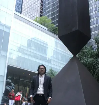 Broken Obelisk sculpture standing in front of modern glass buildings and greenery.