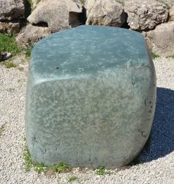 Hattusa Green Stone resting on light gravel beside a rough stone wall and grass