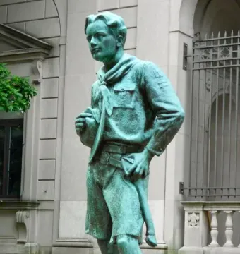 The Ideal Scout statue of a youth in uniform on a stone pedestal outdoors.