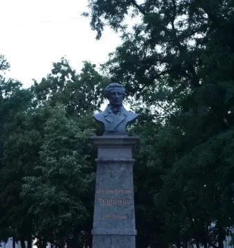 Bust of Pushkin on a tall stone monument beside a bed of yellow flowers.