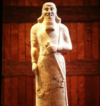 Statue of Ashurnasirpal II with a stylized beard, curly hair, and a long staff held vertically across the body.
