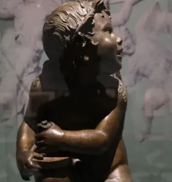 Candelabra Angels, a bronze winged putto seated on an ornate white base and holding a small object while looking upward.