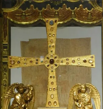 The Cross of the Angels, a jeweled golden cross displayed in a case with two kneeling angel figures beside it.