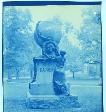 Daguerre Memorial with a bust, globe, and draped female figure on a pedestal in a park