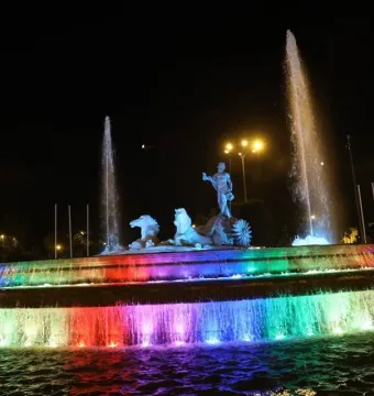The Fountain of Neptune lit with rainbow-colored water jets at night.