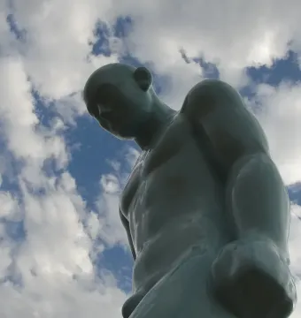 Greetingman statue seen from below against a blue sky with clouds