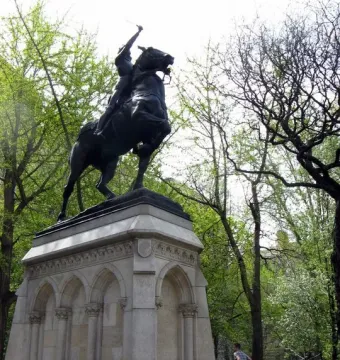Joan of Arc equestrian statue on a tall stone pedestal surrounded by trees.