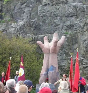 La Mano sculpture with a crowd gathered in front of it, some holding red flags.